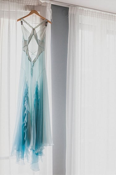 A blue wedding dress hanging in a window.