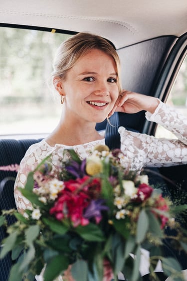 Porträt einer jungen Braut im Auto, die ihren Brautstrauß hält.