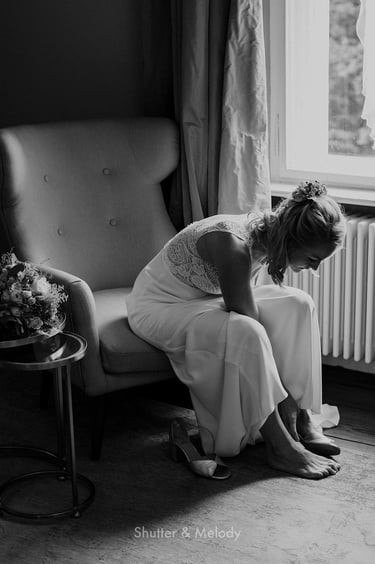 Braut sitzt auf einem Sessel und zieht ihre Schuhe an.
