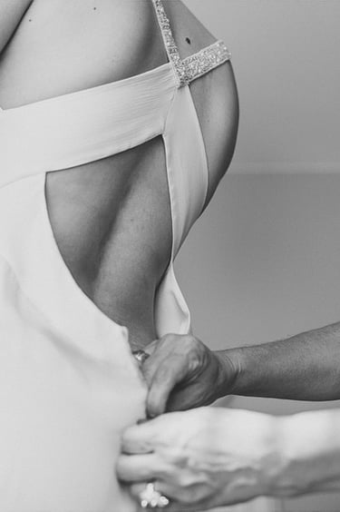 Ein Freund zieht das Kleid der Braut von hinten zu.