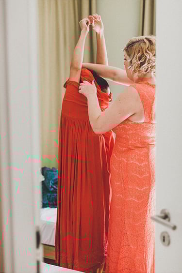 Bridesmaid helping another bridesmaid put on her red dress.