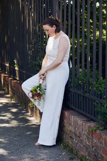 Bride waering pants leaning against a fence. 