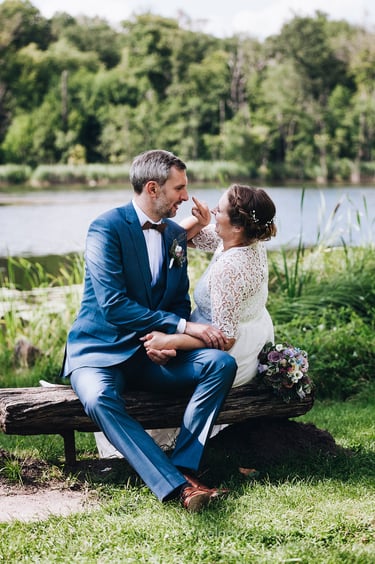 Bride about to touch grooms nose while they sit on a bench.
