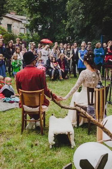 Bride and groom sitting on chairs holding hands and facing their guests.