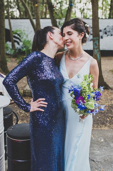 A friend of the bride's in a dark blue sequin dress kissing her on the cheek.