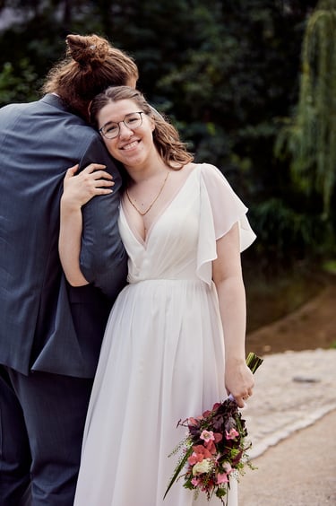Bride leaning on grooms arm holding flowers and smiling.
