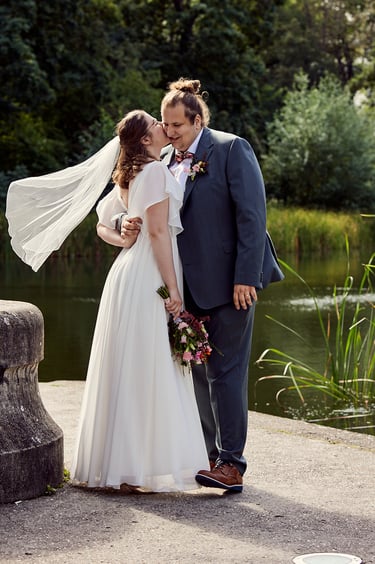 Bride kissing groom on a cheek with her veil floating in the wind.