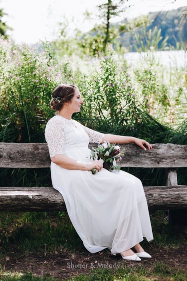 Bride sitting on a wooden bench holding flowers.