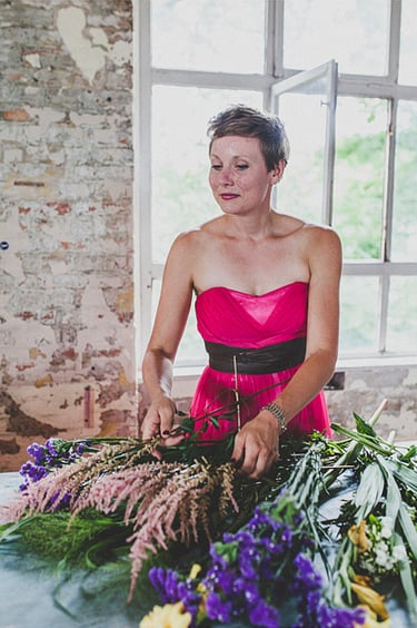 A bridesmaid in a pink dress arranging flowers on a table.