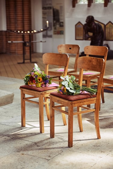 Two chairs in a church with flowers on them.
