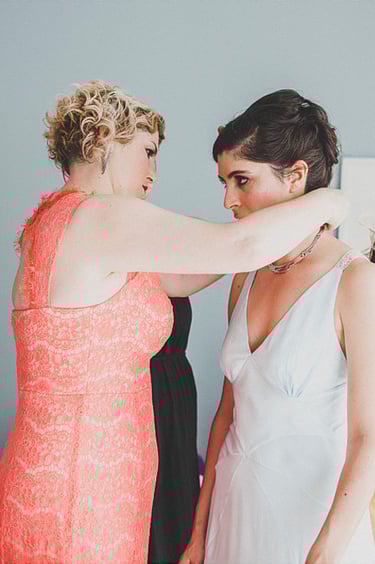 A bridesmaid putting on a necklace on a bride's neck.