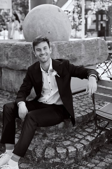 Black and white portrait of a groom sitting on stone steps.