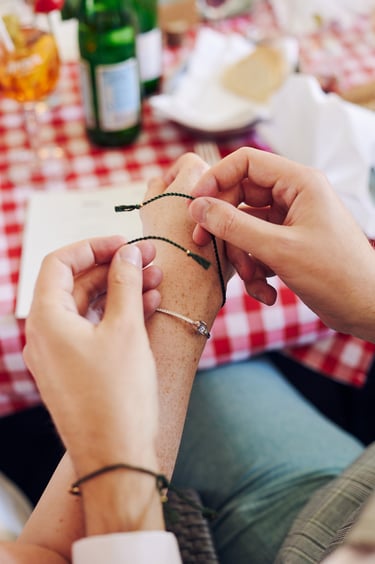 Groom tying up a green cord around bride's wrist.