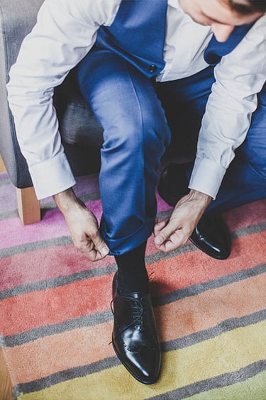 Groom tying his shoes on a colourful carpet.