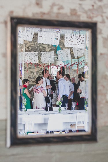 Wedding guests reflected in a mirror, standing next to the table.