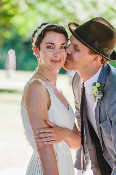 Groom wearing a hat kissing bride on the cheek.