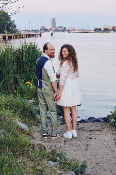 Smiling newlyweds stading at a bank of a river.