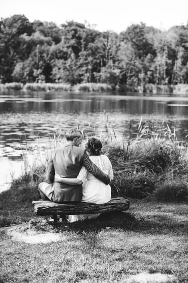 Braut und Bräutigam sitzen auf einer Holzbank mit Blick auf einen See.