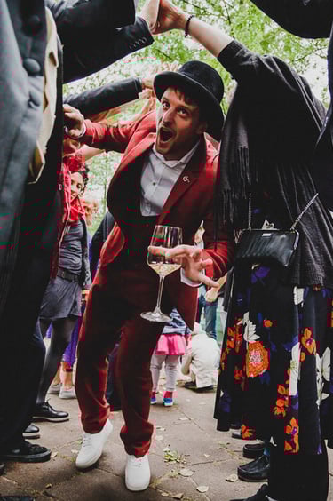 Groom in a red suit passing through a human tunnel.