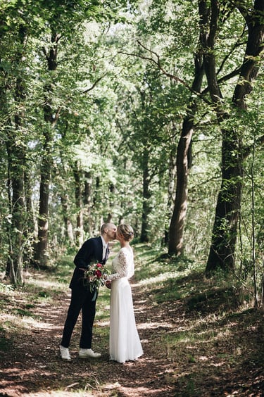 Braut und Bräutigam stehen auf einem Pfad im Wald und küssen sich.