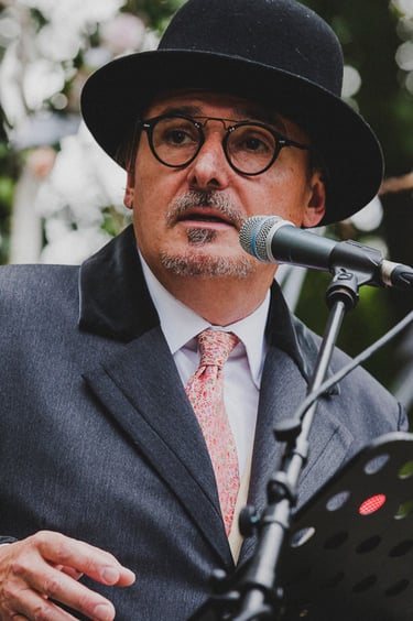 A wedding officiant wearing a hat speaking into a microphone