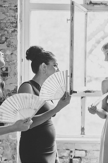 Bridesmaids cooling off with fans talking to each other.