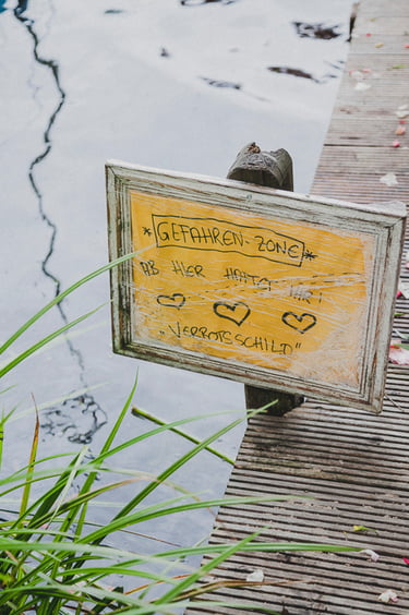 A yellow sign on a pier by a lake.