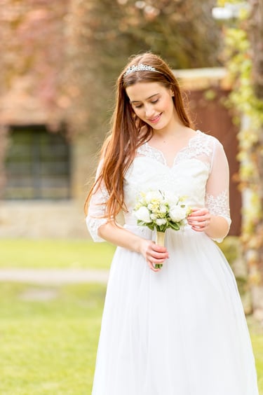 bride in white dress, backlight, blurry autumn leaves background, bride holding bouquet and looking at bouquet
