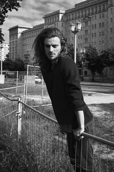 A man with long leaning on a fence in Karl Marx Allee.