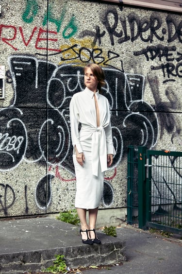 Eine Frau in einem weißen Kleid steht vor einer Wand mit Graffiti.