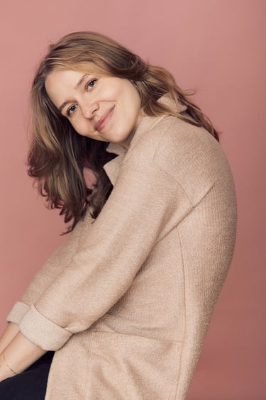 A blonde woman photographed in front of a pink background.