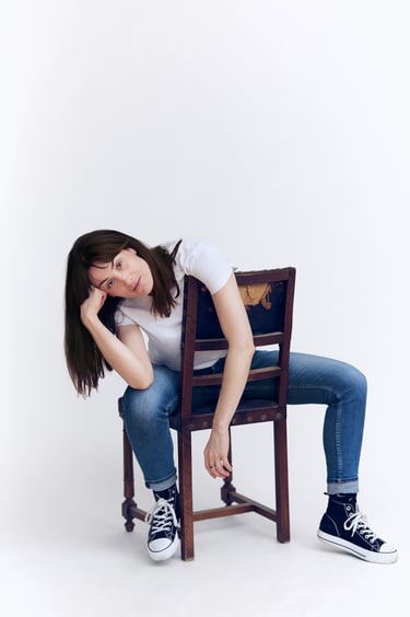 Junge Frau in T-Shirt und Jeans auf einem Stuhl sitzend.