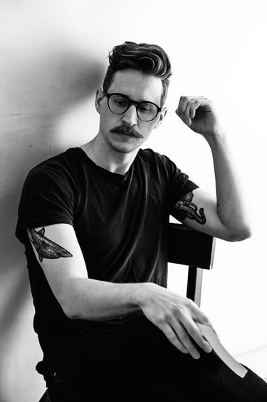 Ein Mann mit Tattoos, der eine Brille trägt und ein Buch in der Hand hält.