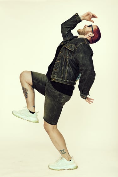 Ein schreiender und springender Mann in Jeansshorts und Jacke.