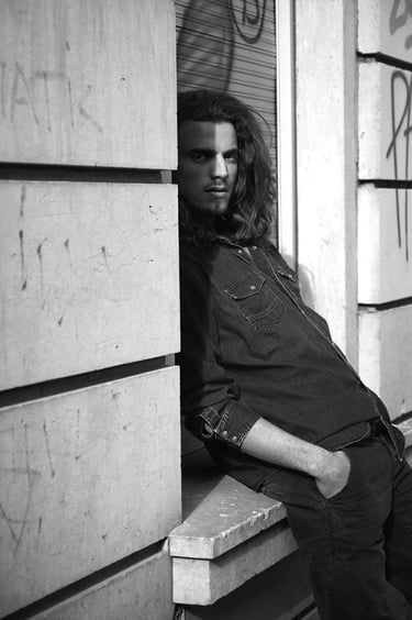 A man with long hair leaning on a building.