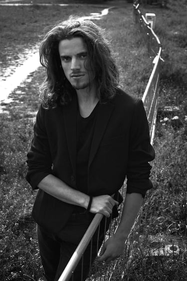 An actor wearing a black jacket and long hair.