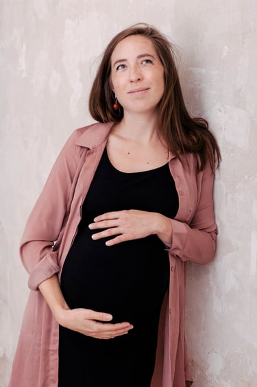 A pregnant woman in a black dress leaning against a wall.