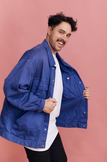 Ein junger Mann mit Schnurrbart, der eine blaue Jacke trägt.