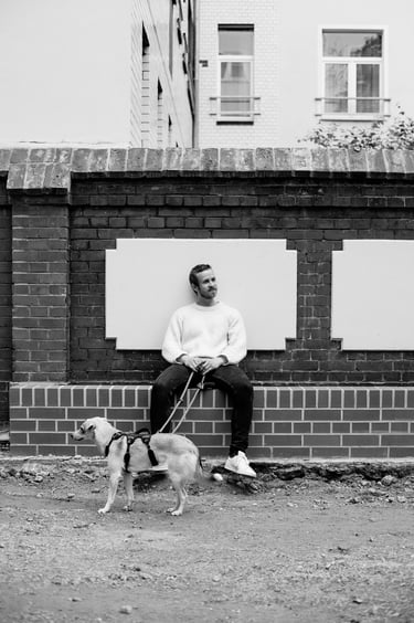 A man sitting on a brick ledge holding a dog leash.