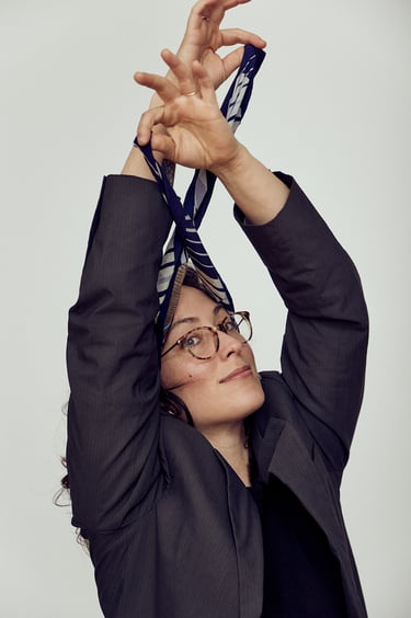 A young woman wearing a suit jacket pulling a scarf over her head.