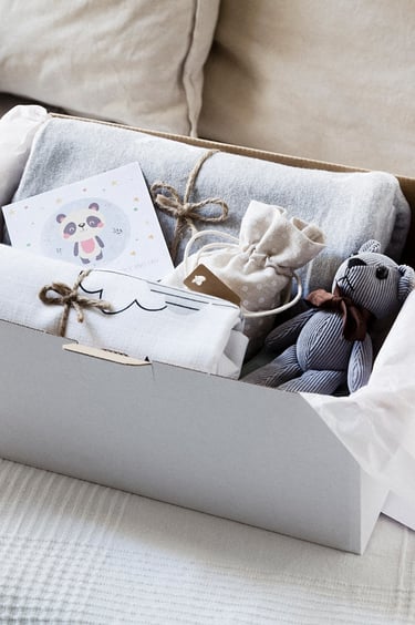 A box with a bear, card, bag, blanket and a towel.