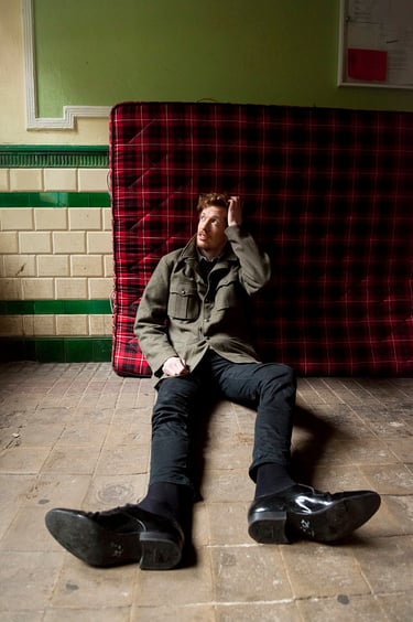 Portrait of a musician sitting in a hallway leaning on a mattress.
