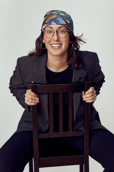 A young smiling woman wearing a floral headscarf sitting on a chair.