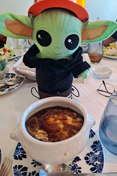 Little green companion wearing a black suit standing in front of bowl of French onion soup