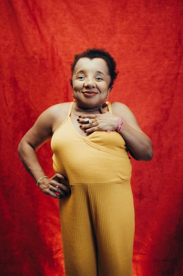 Foto de Roberta Holiday. Mulher negra com nanismo, de cabelos crespos curtos, macacão amarelo.