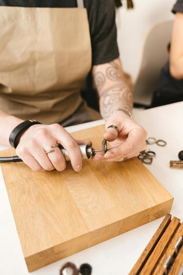 Artesano tatuado utilizando una herramienta rotativa para pulir joyería en un banco de trabajo de ma
