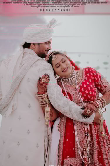 Romantic Indian wedding couple pose, bride in red lehenga leaning on groom in white sherwani. Makeup
