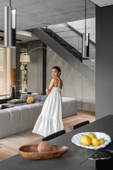 Fotografia wnętrz lifestyle, kobieta w białej sukience na tle betonowych schodów w domu.