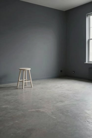 A wide-angle photograph of an empty, minimalist art studio in Buffalo, New York. Featuring dark grey walls and an off-white stool under a single soft studio light. Generous whitespace and a serene, professional atmosphere.