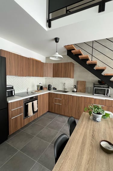 Modern kitchen with wood cabinets, herringbone tile backsplash, and a staircase in a loft apartment.
